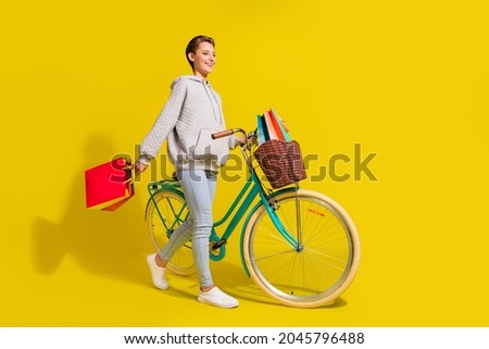 Full length profile photo of cool brown hair millennial lady go with bicecly wear sweater jeans sneakers isolated on yellow background