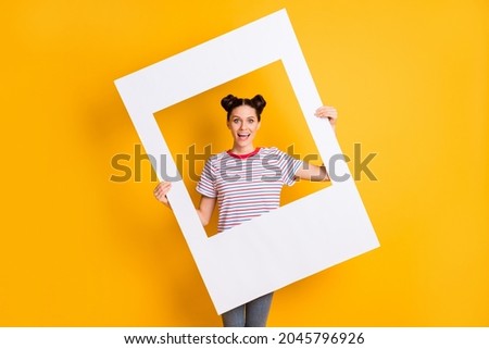 Photo of childish sweet young girl dressed striped t-shirt holding big photo frame isolated yellow color background