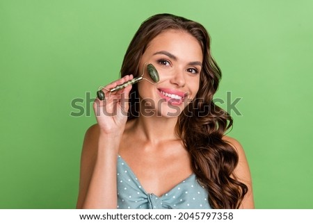 Photo of young attractive girl happy positive smile make face massage lifting roller jade isolated over green color background