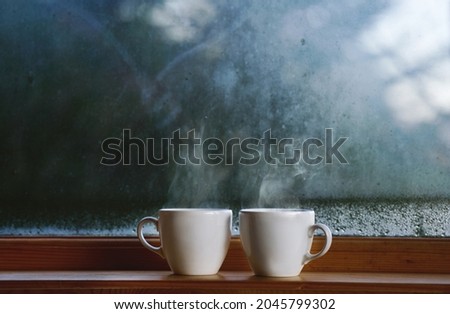 Two cup of hot drink coffee near window, water condensation on window glass, early morning, wake up concept