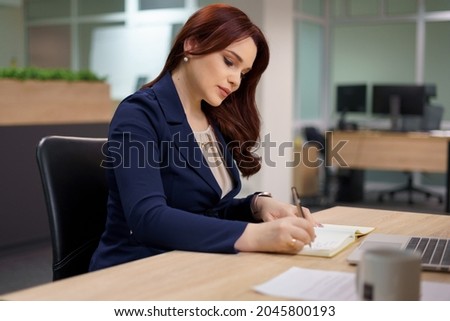 Portrait of businesswoman with laptop writes on a document at her office.
