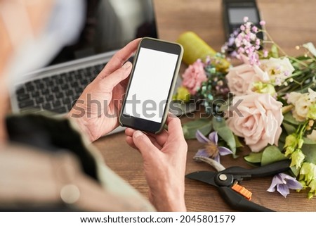 Close up of female small business owner using smartphone with blank screen while managing flower shop, copy space