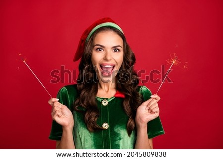 Photo of excited funny young woman dressed elf costume smiling holding bengal fires isolated red color background