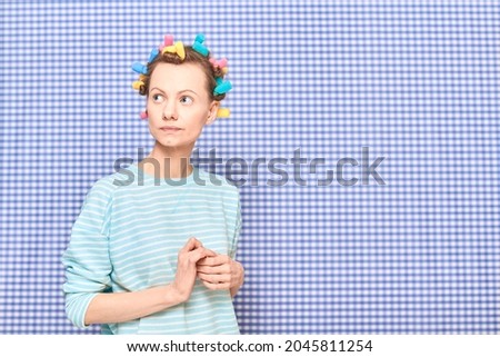 Portrait of thoughtful young woman without makeup with colorful hair curlers on head, looking melancholic and dreamy, standing over shower curtain background, with place for your text and design Royalty-Free Stock Photo #2045811254