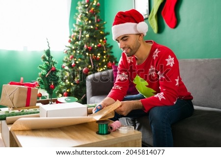 Happy young man using wrapping paper and preparing his christmas gifts before celebrating a party 