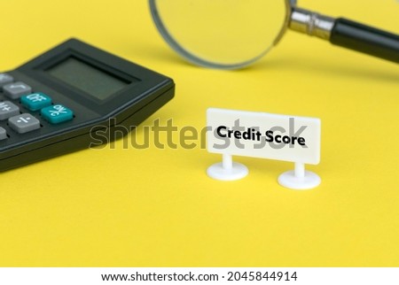 Selective focus of magnifying glass, calculator and white sign board written with Credit Score on yellow background.