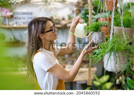 Young female gardener watering potted plant handing. Woman student or professional florist taking care of houseplants in home garden, floral store or orangery. Gardening hobby leisure activity concept Royalty-Free Stock Photo #2045860592