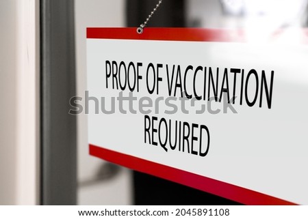 Proof of vaccination required to enter non essential business hanging at window store. Banner of coronavirus vaccine requirement for entering indoors.