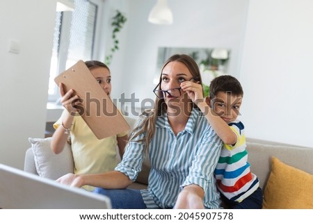 Upset mother having problem with noisy naughty daughter and son jumping on couch and screaming, demanding attention, frustrated mum tired of difficult child trying to work from home Royalty-Free Stock Photo #2045907578