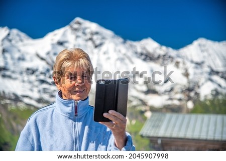 Happy retired elderly woman taking pictures of a beautiful summer mountain landscape