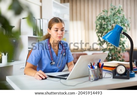 Young woman doctor is working at a computer, sitting at workplace in the resident's office in the medical clinic Royalty-Free Stock Photo #2045914493
