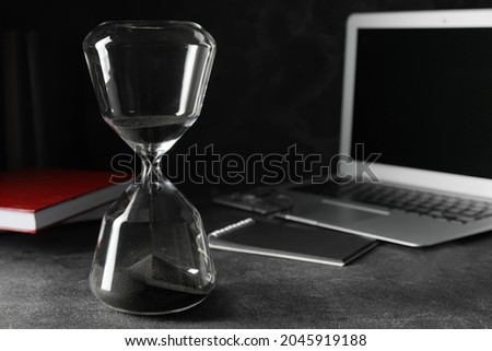 Stylish hourglass and laptop on dark table in office. Deadline concept