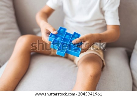 Boy lying on the couch and playing with sensory pop it fidget toy at home. Kid playes stress and anxiety relief fidgeting game. Boy with pop it a heart shape sensory toy. 