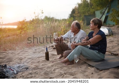 Senior couple Camping holiday in the summer nature. Camping concept. elderly people drink wine on the beach near the fire on a summer evening
