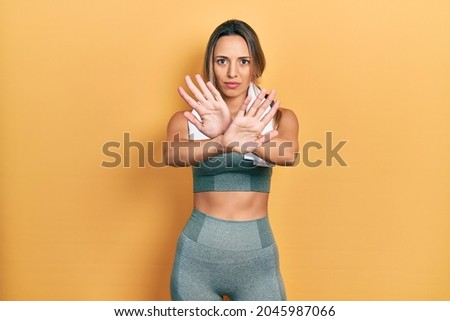 Beautiful hispanic woman wearing sportswear and towel rejection expression crossing arms doing negative sign, angry face 
