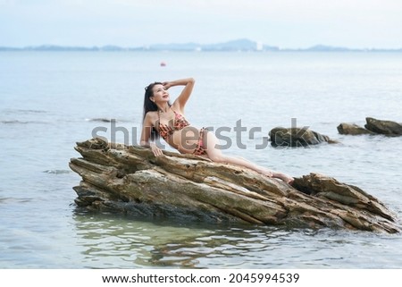 Beautiful woman in orange bikini sitting on rocks at beach, leisure activities,holiday vacation.