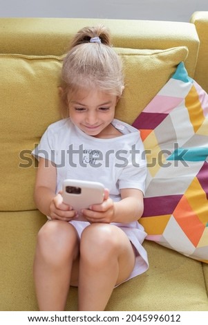 little girl watching cartoons on smart phone. Kid girl sit on couch hold gadget spend time on internet fun website for children.