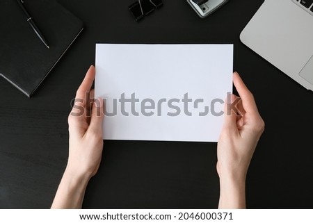 Woman holding blank sheet of paper on dark background