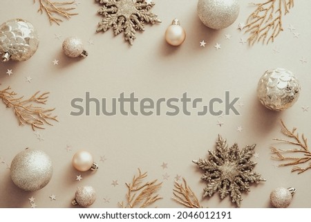 Christmas frame with golden snowflakes, Xmas tree branches, balls on beige background. Flat lay, top view.