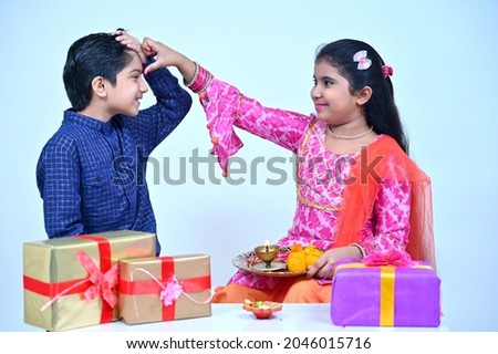 Little girl in tradional clothes performing bhaiya duj rituals on brother, studio shot