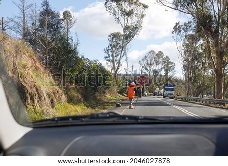 view through a windshield of a man in orange hi-vis clothes holding a stop sign on the road in Adelaide, South Australia
