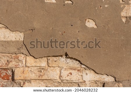 The old wall of the building with cracked plaster from time. The texture of the peeling and peeling surface of the brickwork.