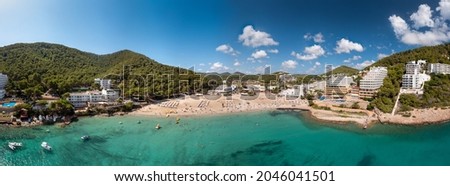 Large format wide angle panoramic aerial photo of the Spanish island of Ibiza showing the beautiful beach front and holiday hotels at the beach of Cala Llonga in the summer time, on a sunny day