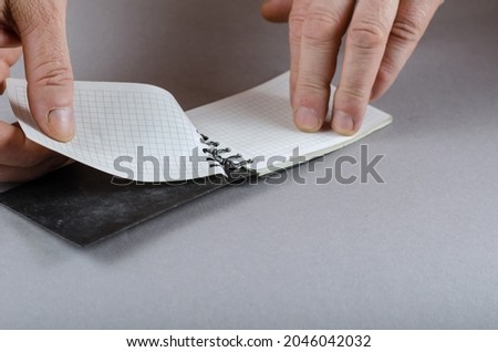 Hands wresting sheet of paper out of spiral notebook. Adult male. Gray background. Close-up. Selective focus.