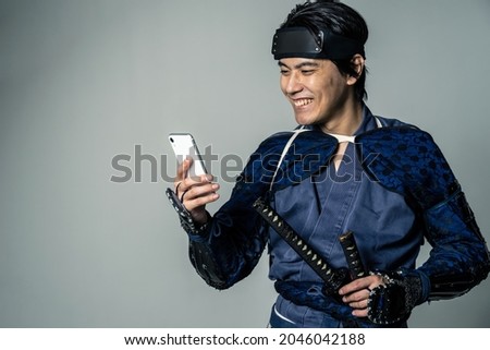 Smiling Japanese armed samurai who uses a smart phone.