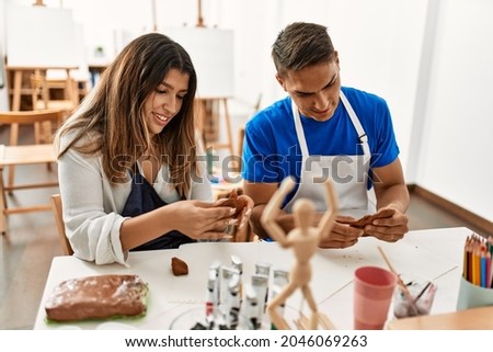Two students smiling happy modeling clay sitting on the table at art school.
