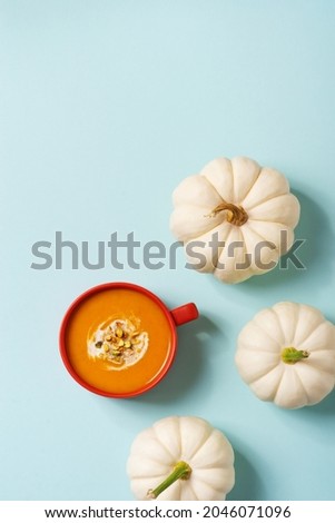 Autumn pumpkins soup in orange plate with vegetables on blue background, modern concept, copy space, vertical