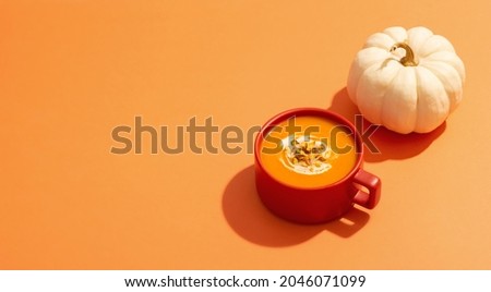 Autumn pumpkins soup with vegetables on orange background, modern concept, copy space