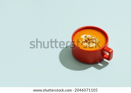 Autumn pumpkins soup in red orange bowl or cup on blue background, modern concept, minimalism, copy space