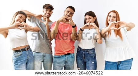 Group of young friends standing together over isolated background smiling in love doing heart symbol shape with hands. romantic concept. 