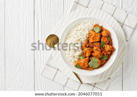 butter chicken with long grain rice and coriander, tandoori chicken in a tomato gravy, rich in butter and cream in a bowl on a white wooden table, english cuisine, flat lay, free space Royalty-Free Stock Photo #2046077051