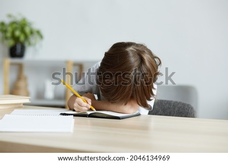 Exhausted school kid is tired from homework and learning and is lying on the desk. Difficulties in children's learning and problems with school tests and exercises. Overwork and stress in preschool.