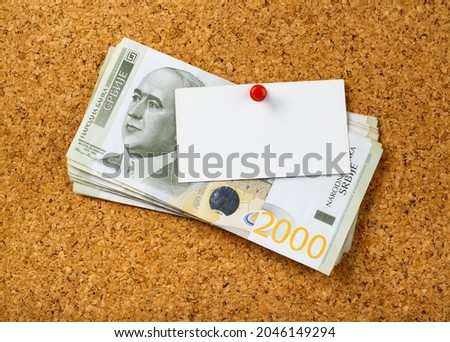 Stack of two thousand Serbian dinar bills hanging on cork board with thumbtack and blank note for Your message.