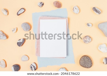 Blank white sheet template with notebook on beige background with natural stones, flat lay