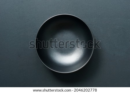 On a black hardwood background, a top view of a black empty round ceramic bowl. Royalty-Free Stock Photo #2046202778