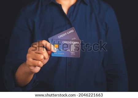 Midsection of a businessman in a blue shirt holding a mockup blue credit card while standing with a black background in the studio. Close-up photo. Money and business concept.