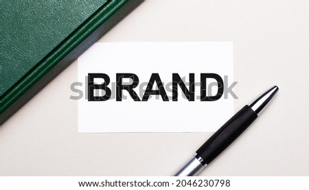 On a light gray background lies a pen, a green notebook and a white card with the text BRAND. Business concept.