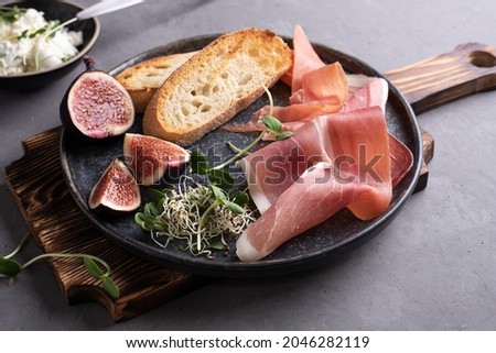 Italian antipasto from prosciutto, toast, cream cheese on a cutting board on a gray background, ham snack, close-up. Royalty-Free Stock Photo #2046282119