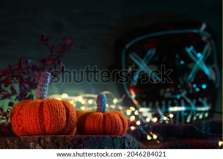 Knitted Halloween orange pumpkins, glowing creepy neon mask on a dark background, copyspace greeting card