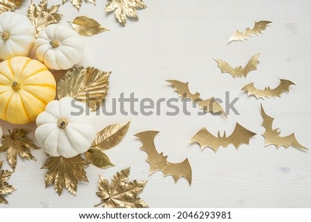 Sweet mini pumpkins, golden autumn leaves and bats on a white wooden table with copy space. Halloween decor with copy space.