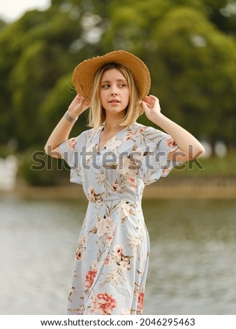 A beautiful young European girl in a blue dress and a straw hat is resting in the park: walking, taking pictures and feeding birds. Weekend in the city