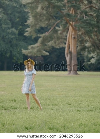 A beautiful young European girl in a blue dress and a straw hat is resting in the park: walking, taking pictures and feeding birds. Weekend in the city