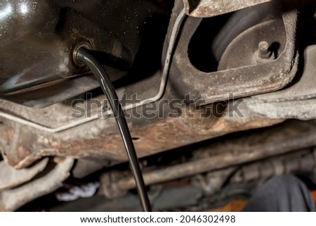 Old and dirty oil is drained from the underchassis of an SUV. Maintenance procedure of a diesel vehicle. Royalty-Free Stock Photo #2046302498