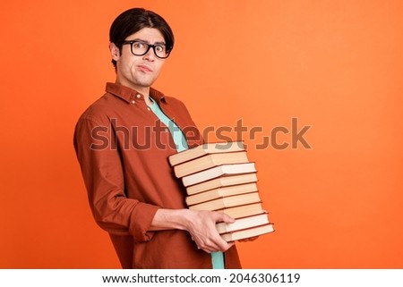 Photo of unhappy upset young college student geek nerd hold heavy stack books wear glasses isolated on orange color background