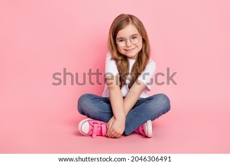 Photo of cute lovely small girl sit floor hands hold wear specs white t-shirt jeans shoes isolated pink color background