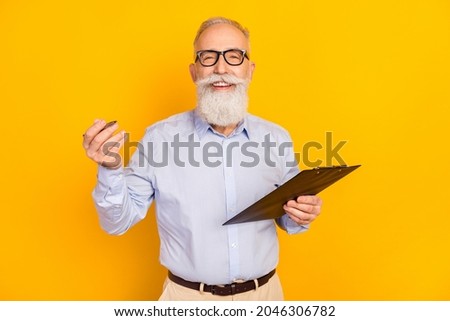 Photo of charming old happy positive old man hold pen clipboard smile wear glasses isolated on yellow color background